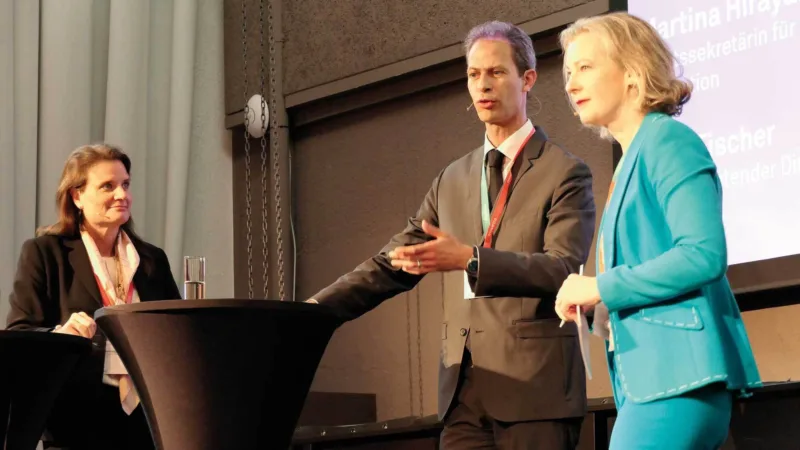 Martina Hirayama, Yves Fischer und Katrin Frei stehen um einen Tisch und sprechen miteinander.