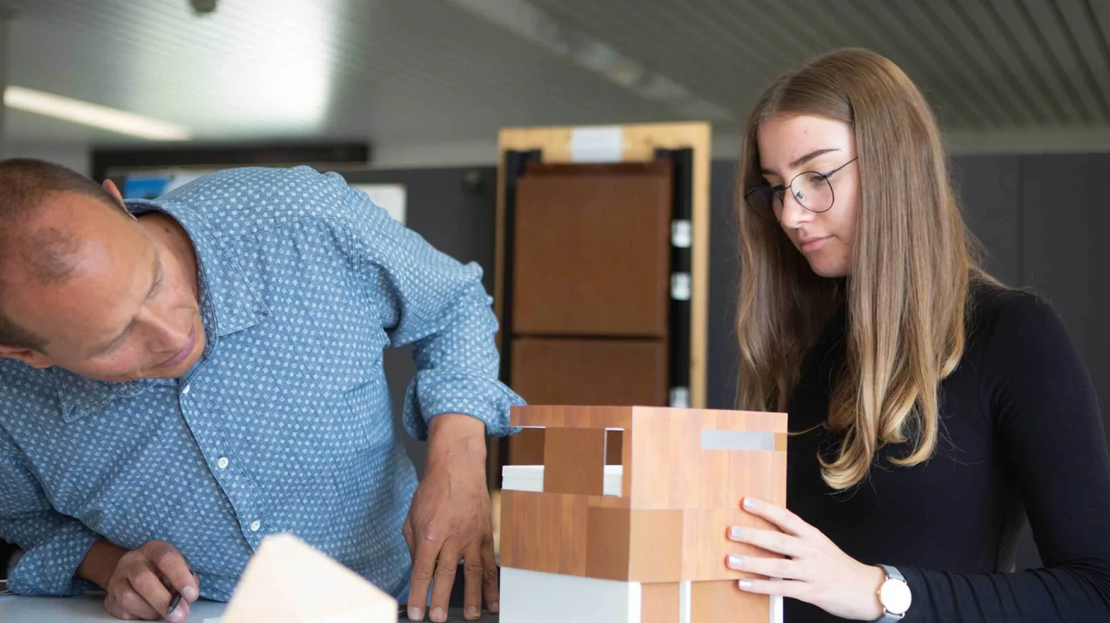 An apprentice and her colleague work on a paper model