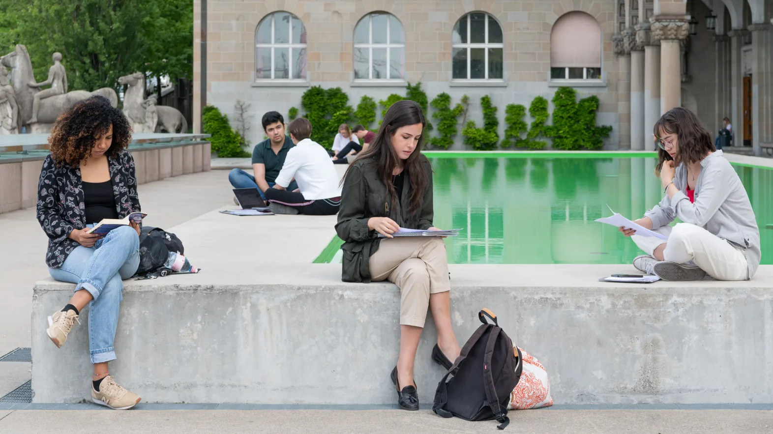Étudiants assis en train de lire devant un bâtiment de l'université de Zurich