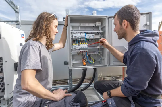 A vocational training supervisor explains something to an apprentice in a fuse box.