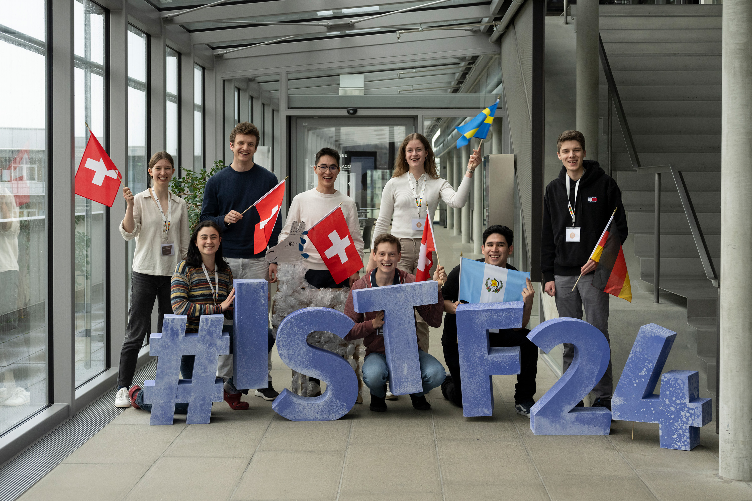 Eight talents pose with the blue letters and signs #ISTF24 and flags of their countries of origin