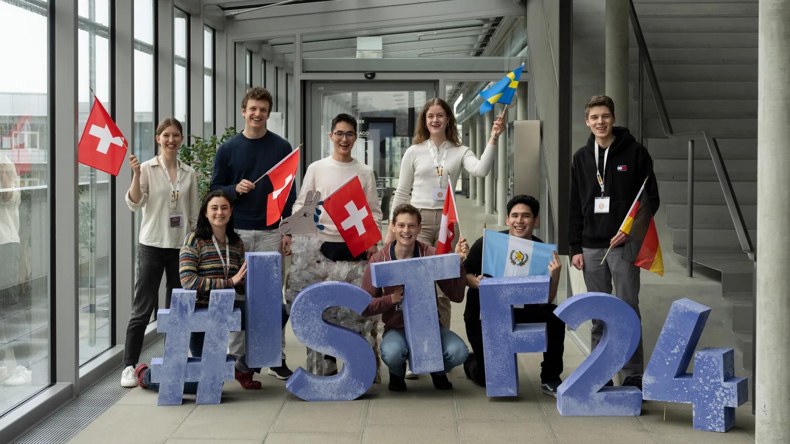Huit talents posent avec les lettres et signes bleus #ISTF24 et les drapeaux de leurs pays d'origine