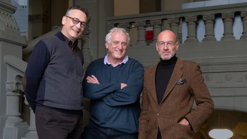 Three men stand in a stairway smiling.
