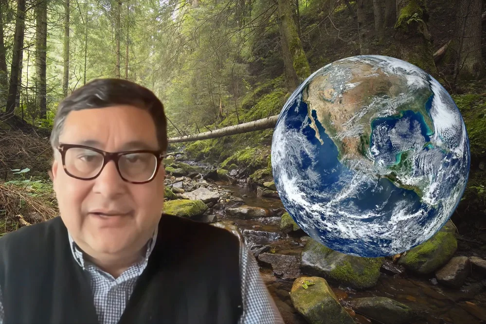 A man wearing glasses speaks against a virtual background of a forest, with an image of earth from space next to him.