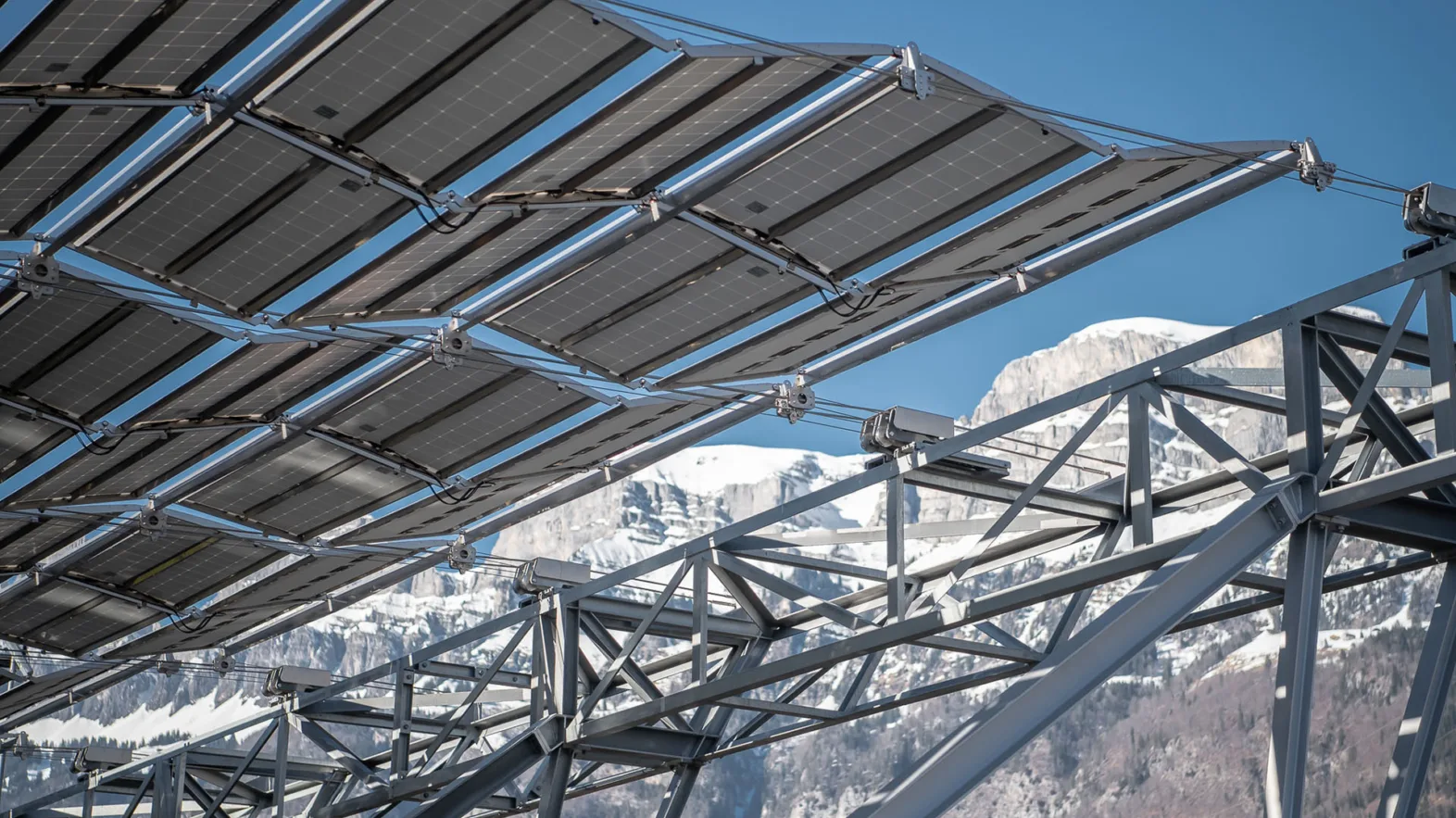 Foldable solar panels against a backdrop of snowy alps and a blue sky on a sunny day.