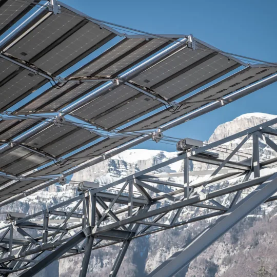 Foldable solar panels against a backdrop of snowy alps and a blue sky on a sunny day.