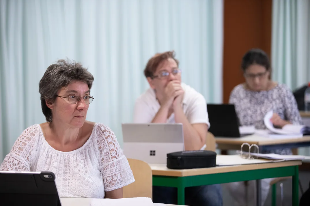 Une femme en T-shirt blanc devant un ordinateur portable dans une classe pour adultes.