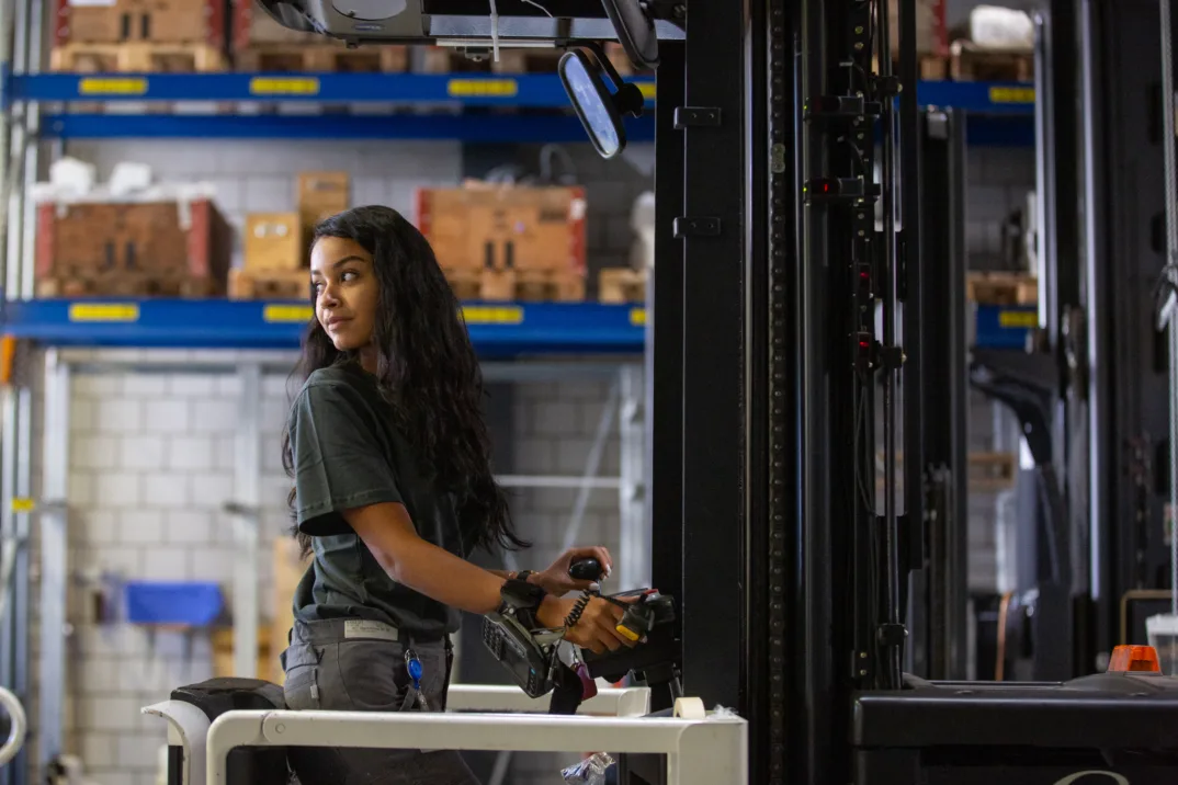 A young woman with long black hair drives a forklift.