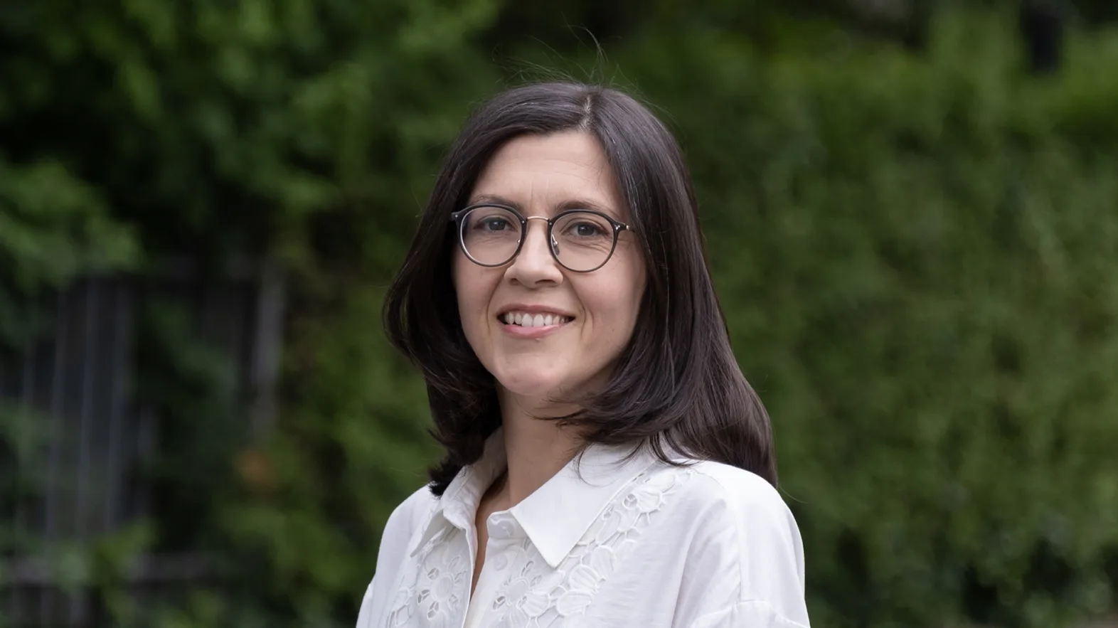 Portrait of a woman wearing a white blouse and glasses with shoulder-length black hair.