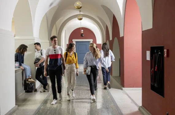 Students walking down a hallway with arches and red and white walls.