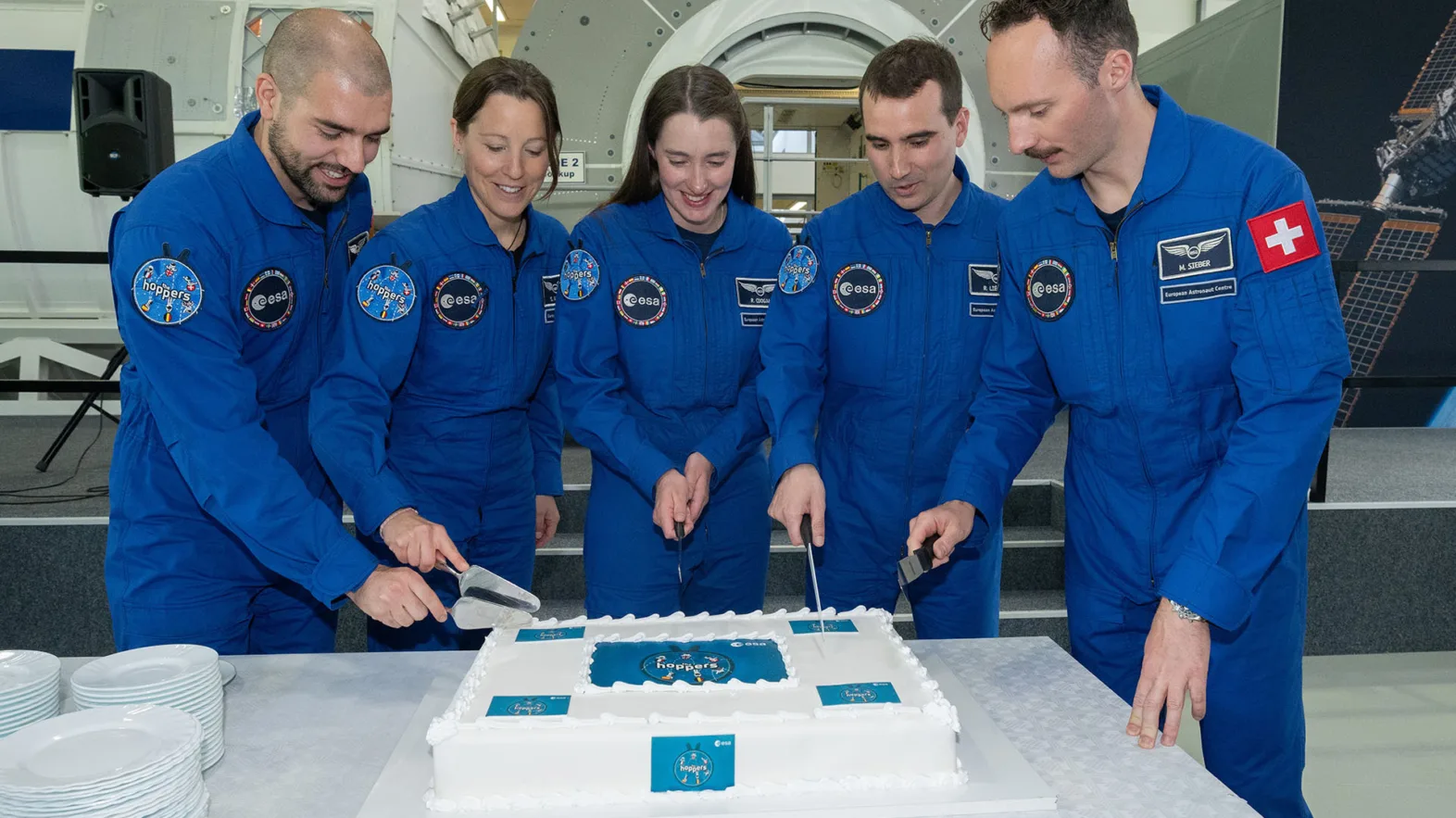 Die fünf ESA-Astronautinnen und -Astronauten schneiden gemeinsam ihren Kuchen zur absolvierten Grundausbildung an.