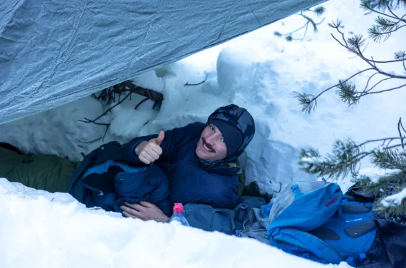 Marco Sieber lies smiling in the snow in his winter clothes and gives a thumbs up.