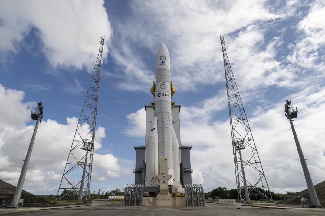 Die Ariane 6-Rakete auf ihrer Startrampe vor einem blauen und bewölkten Himmel.