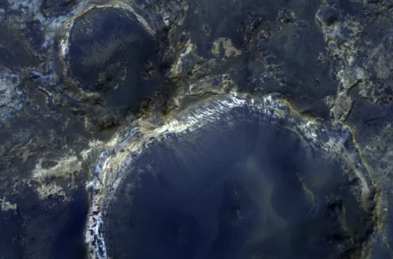 A photo of large craters on mars. They are blue with white and yellowish rims.