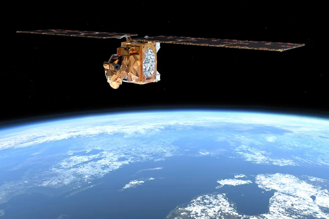 A copper-colored satellite with large wings flies in space with the largely ocean-covered surface of the Earth below it.