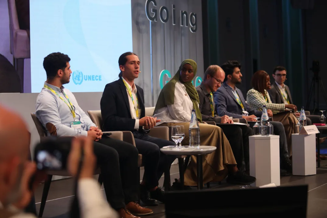 Young people sit in a row on a stage in front of white tables.