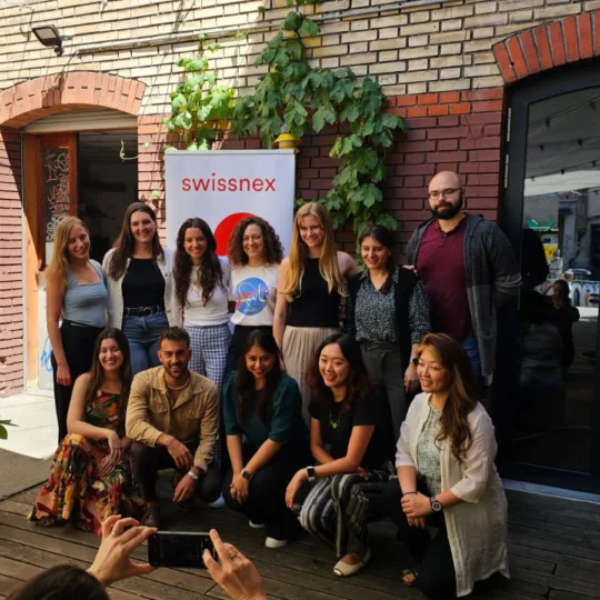 A group of people pose for a picture in a courtyard in front of a brick wall and a Swissnex banner.