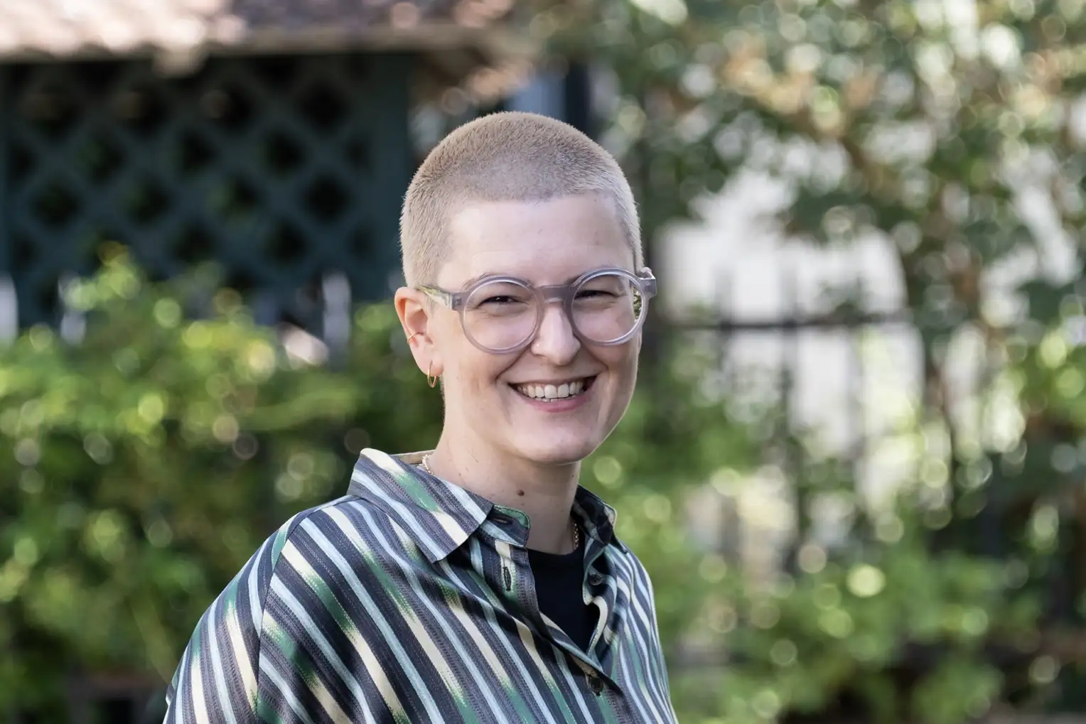 Une femme aux cheveux blonds et courts, portant des lunettes et un chemisier à rayures, sourit à la caméra.