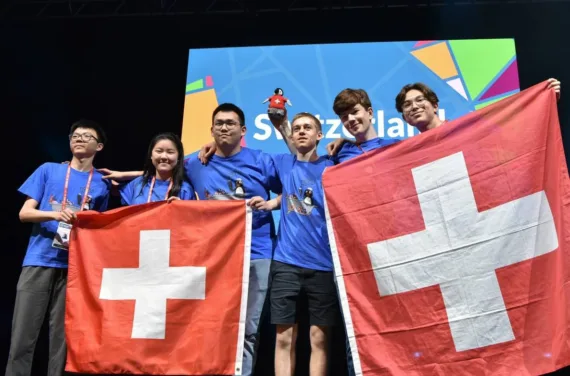 Eine Gruppe von sechs jungen Teilnehmern steht auf einer Bühne und hält zwei große Schweizer Flaggen hoch.