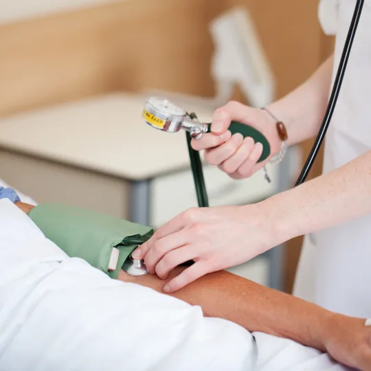 Eine Pflegefachkraft misst den Blutdruck eines Patienten in einem Krankenhausbett.