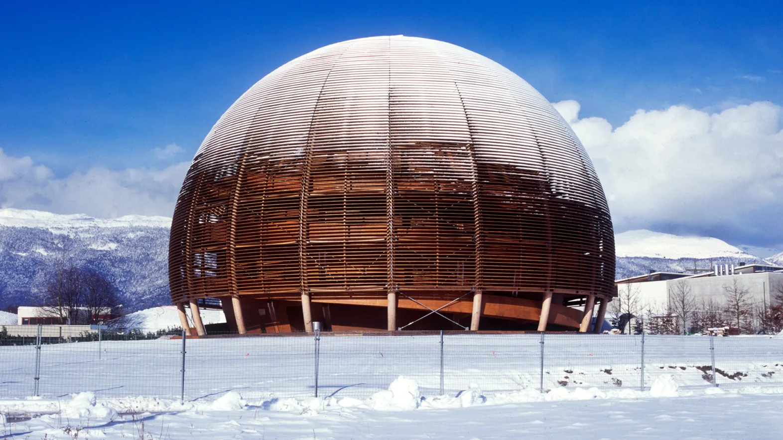 The "Globe of Science" is covered in snow in the middle of a snowy field against a backdrop of snowy mountains and a blue sky.