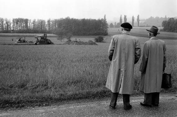 Photographie en noir et blanc de deux hommes debout devant un champ, le dos tourné à l'appareil photo.