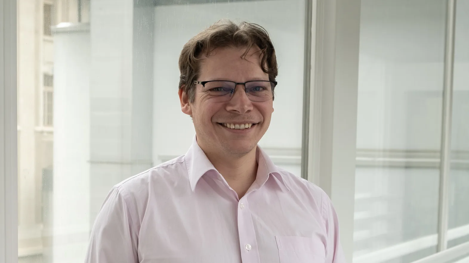 Portrait of a man wearing glasses and a light pink button-down shirt.