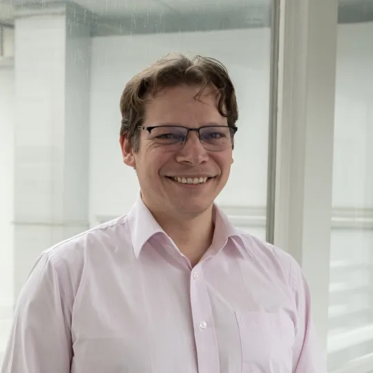 Portrait of a man wearing glasses and a light pink button-down shirt.