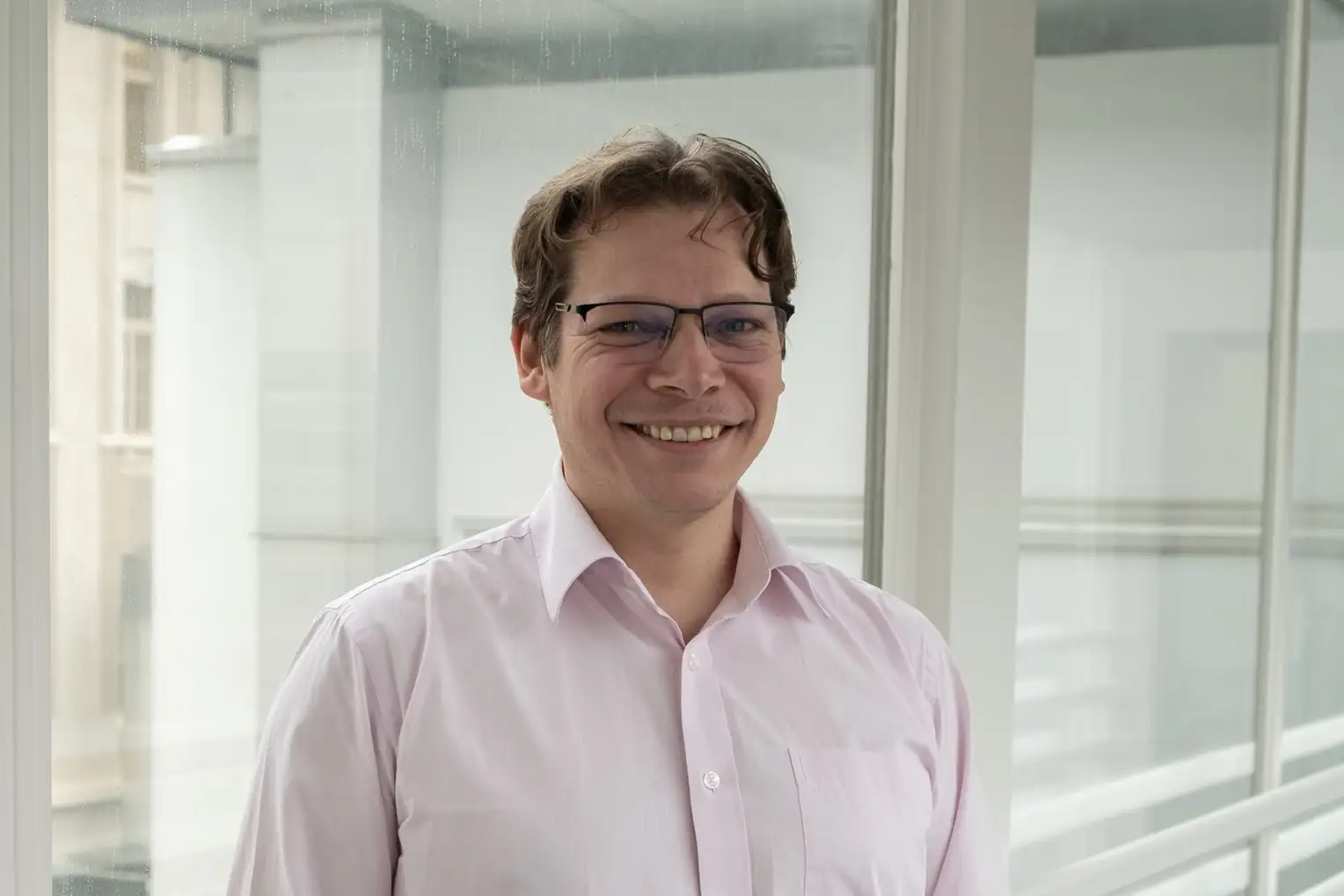 Portrait of a man wearing glasses and a light pink button-down shirt.