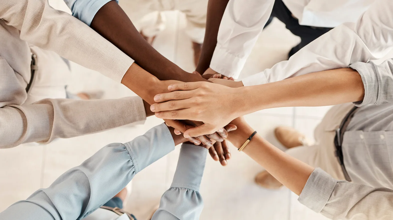 A group of people stand in a circle, holding hands in the middle and crossing them over each other.