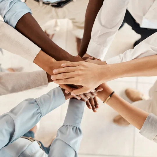 A group of people stand in a circle, holding hands in the middle and crossing them over each other.