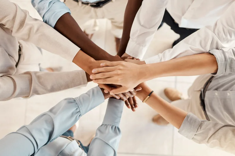 A group of people stand in a circle, holding hands in the middle and crossing them over each other.