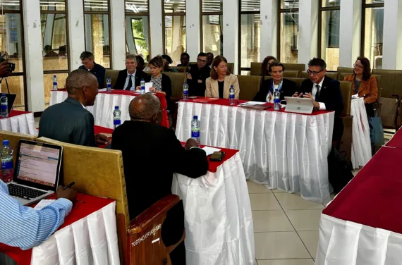 People are sitting at tables with red and white tablecloths in several rows in a conference room.