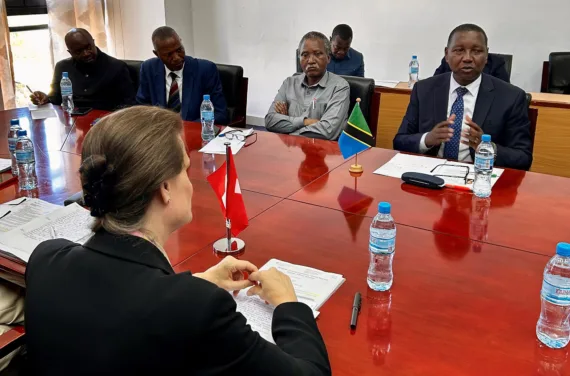 A group of people are sitting at a conference table with paper, bottled water and small flags in front of them.