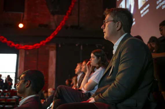 A man in an audience intently follows a presentation.