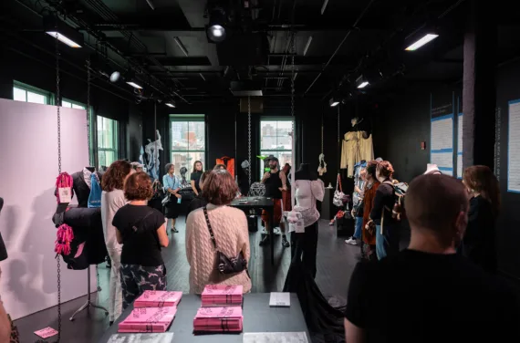 A group of people watches a presenter in a fashion exhibit.