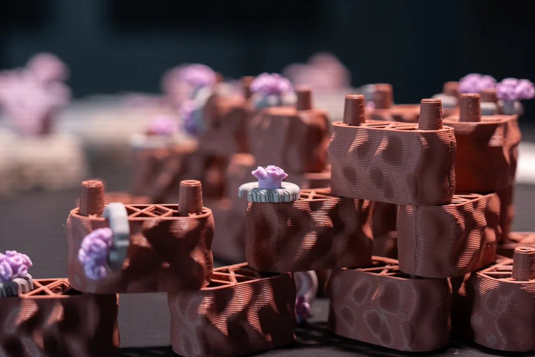 Plastic brown coral reef modules are arranged on top of each other. Each has a gray plastic gear wheel and light purple plastic coral attached to it.