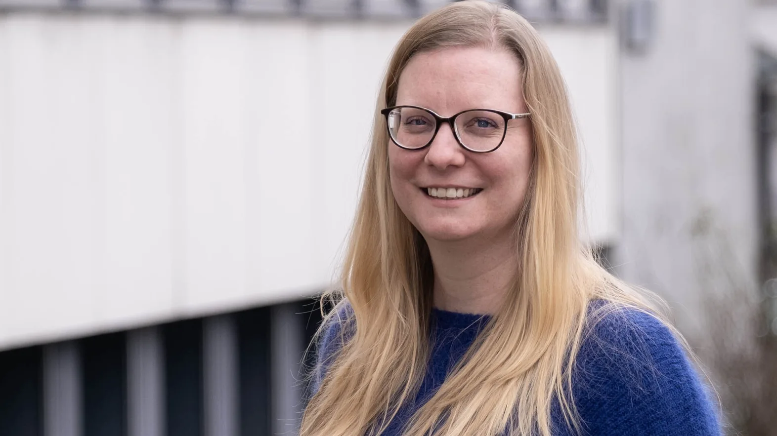 Priska Barghouti ist eine Frau mit blonden Haaren. Sie trägt eine Brille und einen violetten Pullover.