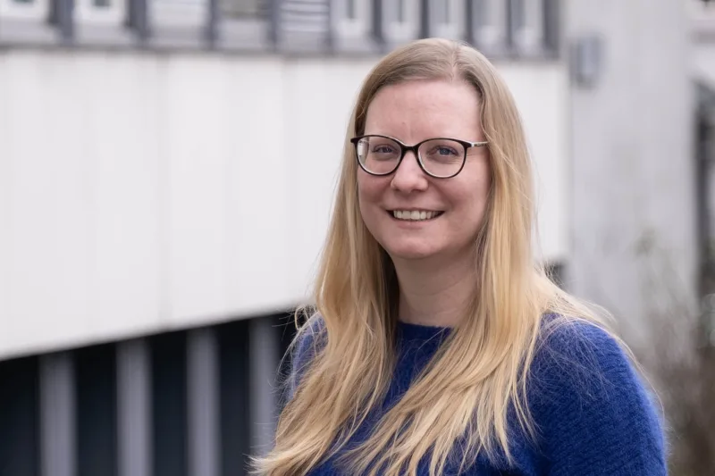 Priska Barghouti is a woman with blonde hair. She wears glasses and a purple sweater.