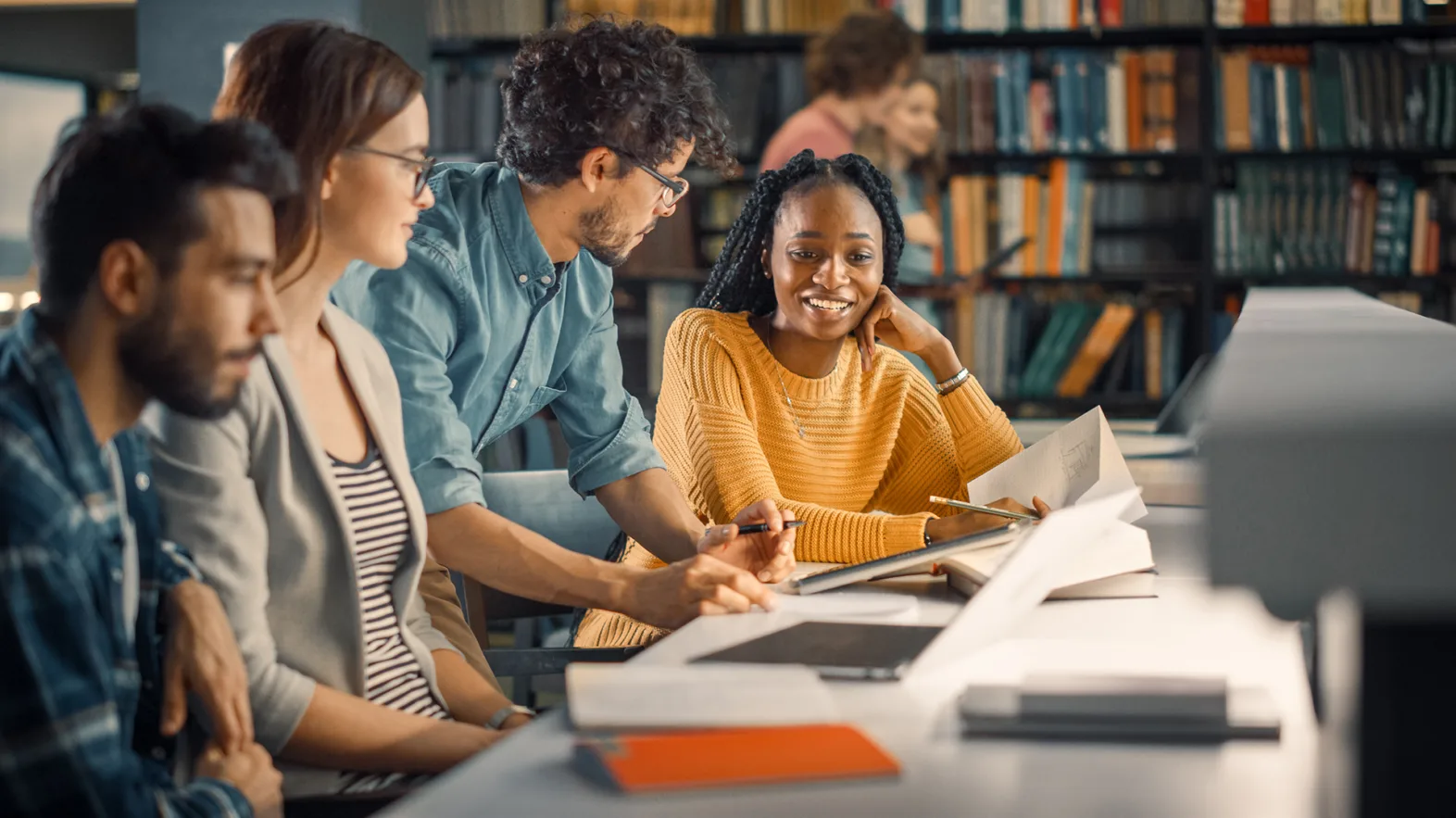 Vier Studierende unterhalten sich in der Bibliothek.