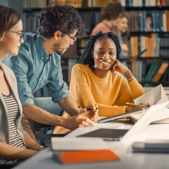 Vier Studierende unterhalten sich in der Bibliothek.