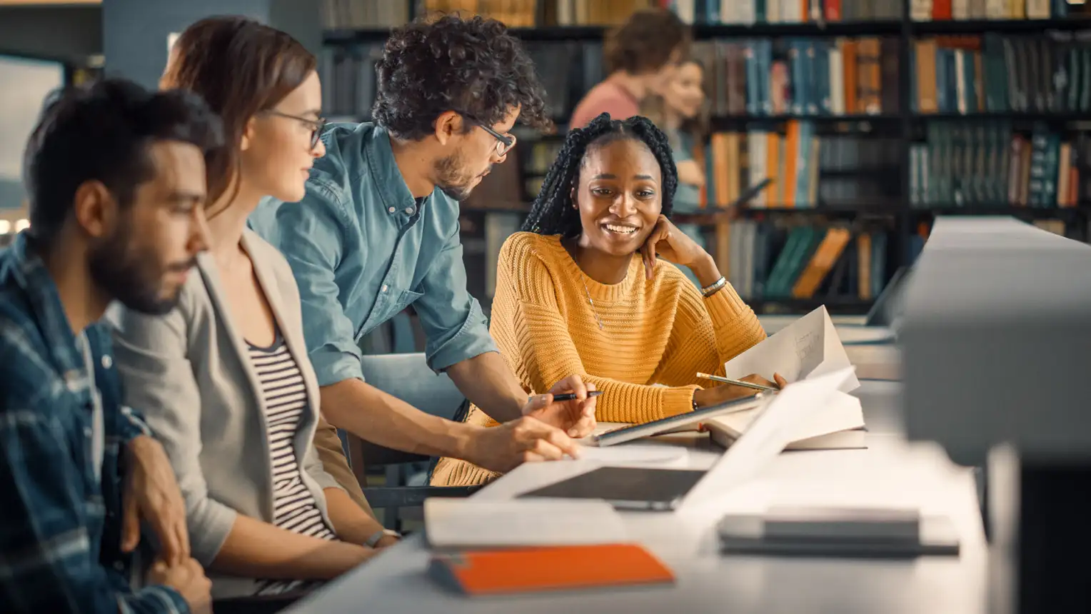 Vier Studierende unterhalten sich in der Bibliothek.