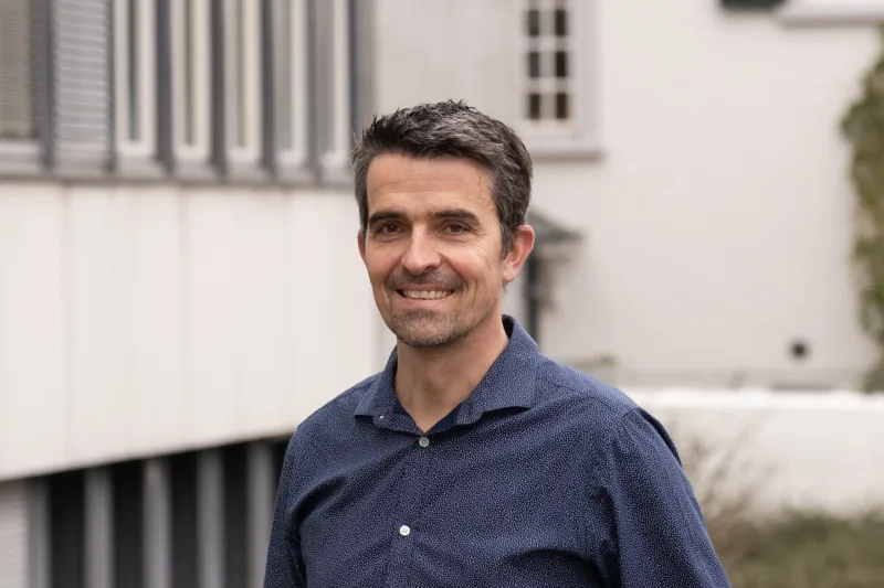 Florian Berset is wearing a blue shirt and standing in front of the SERI building.