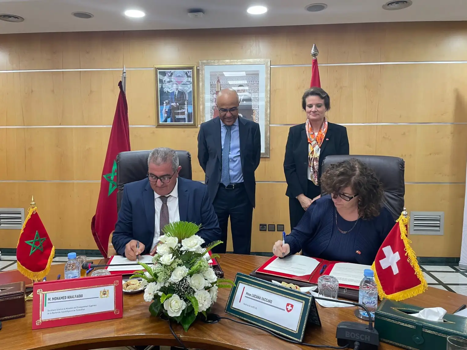 Two people standing behind two seated people who sign an agreement