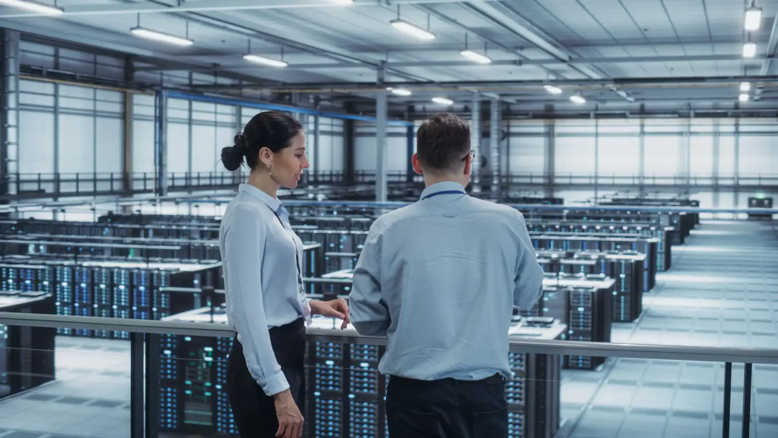 Two people are standing in a large, modern server room looking at numerous rows of servers.