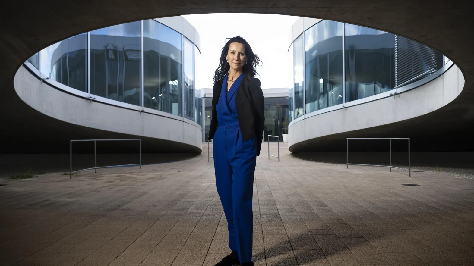 A woman in front of a building, wearing a blue jumpsuit.