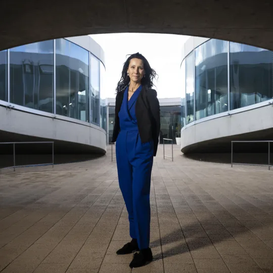 A woman in front of a building, wearing a blue jumpsuit.