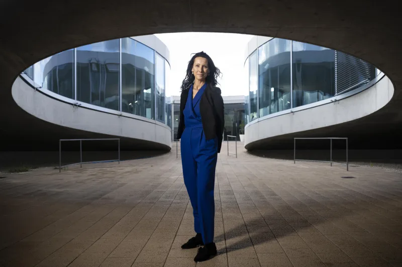 A woman in front of a building, wearing a blue jumpsuit.