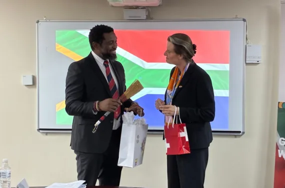 Minister Manamela 25 09 2025 Un homme et une femme se tiennent devant le drapeau sud-africain et discutent.