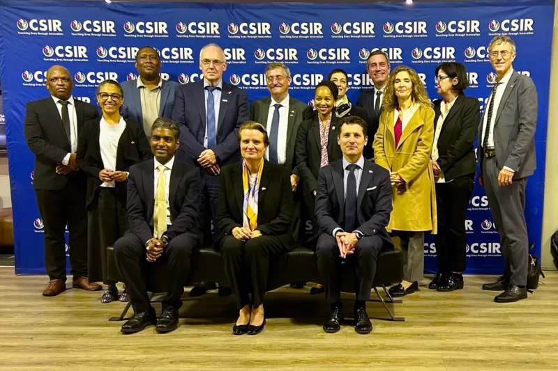 A group of people stand in front of a blue banner and look at the camera.